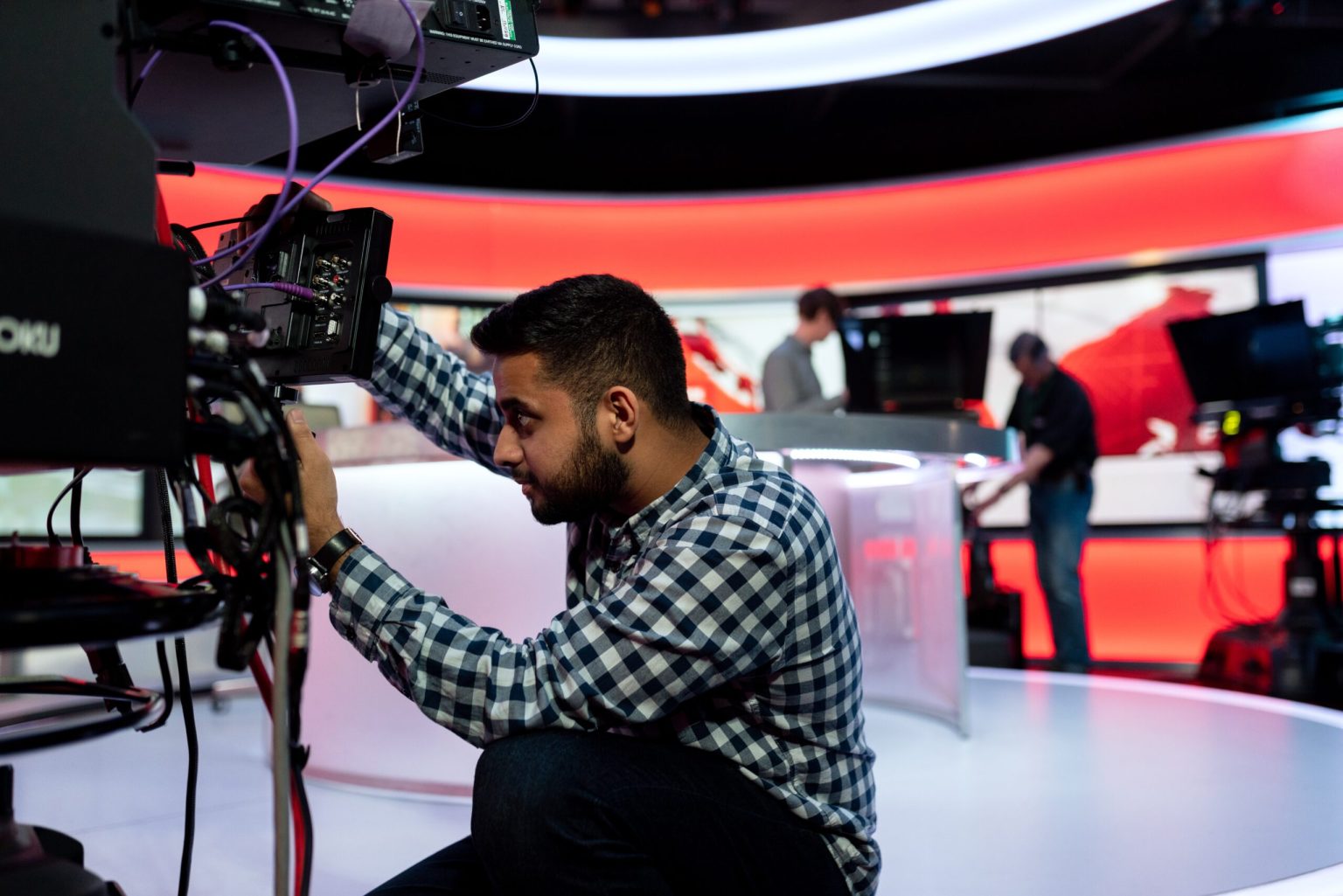 Camera operator kneeling in front of camera in BBC news studio 