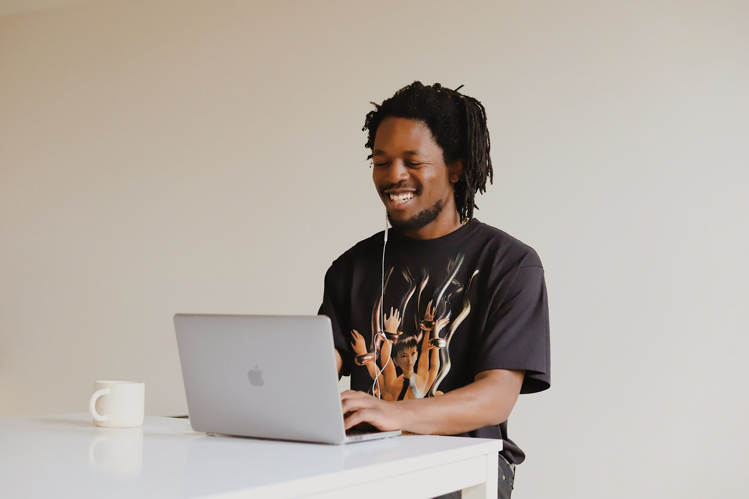 a young black man sits in a white room at a laptop he is smiling and laughing