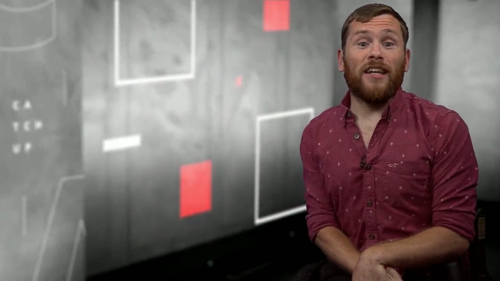 ellis, a man with short hair and a beard, presents the news in a studio. he is in front of a backdrop of squares 
