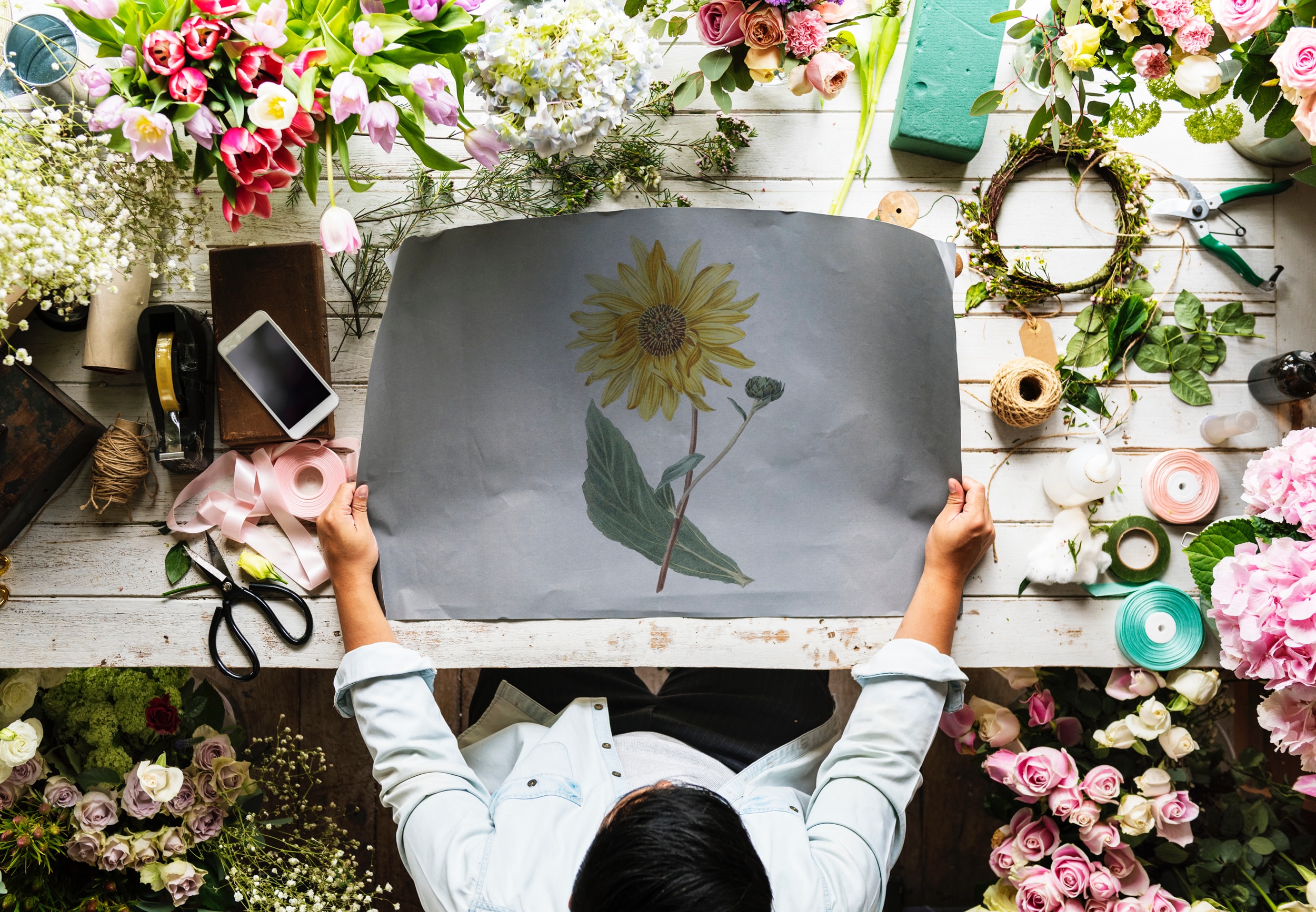 an areil view of a person at a desk holding a painting of a sunflower