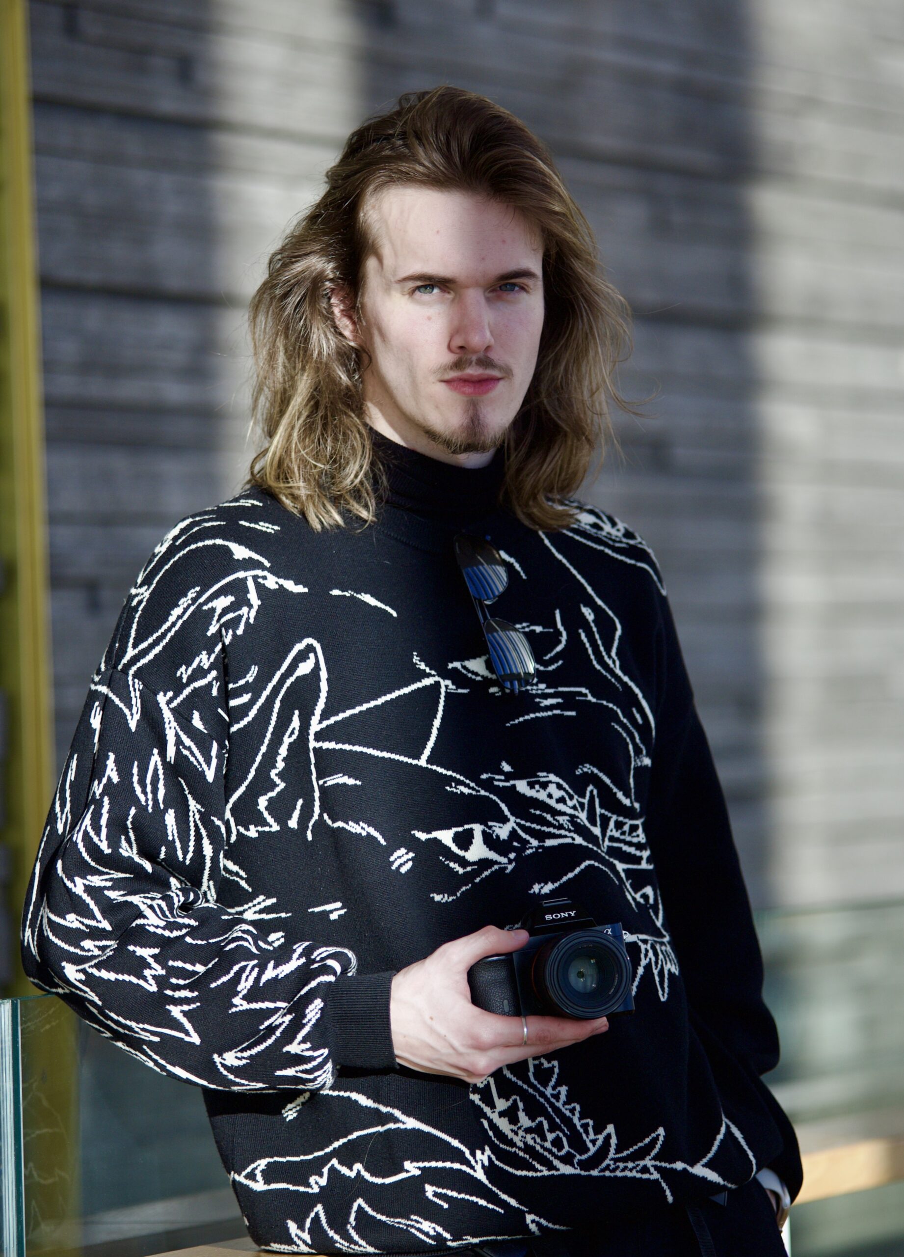 Matteus Labiak, wearing a black jumper and holding a camera, looking to camera
