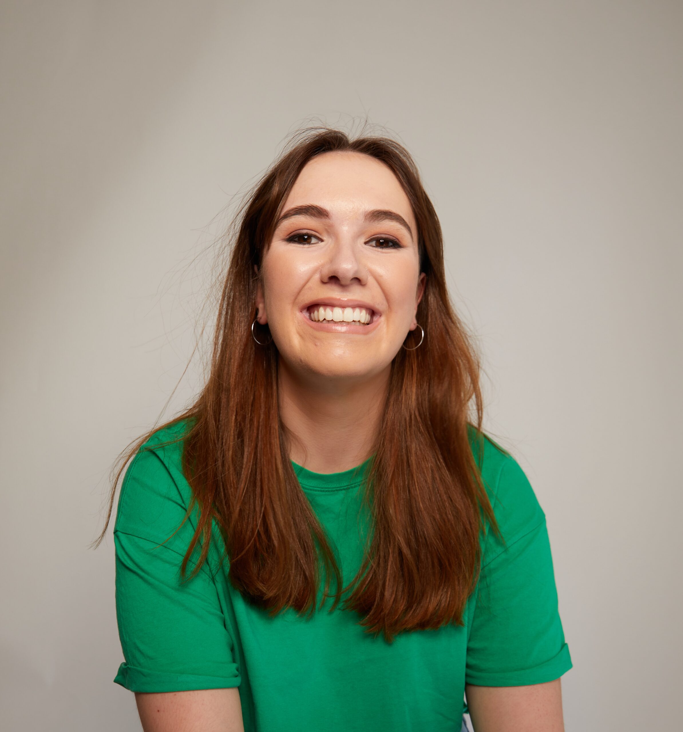 Lucie a woman with brown hair and wearing a bright green top, smiles to camera